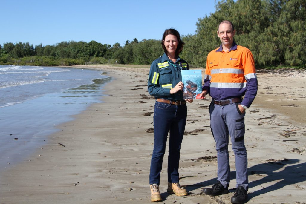 Ricci Churchill and Tim Ffrost standing on a beach with a copy of the Report Card