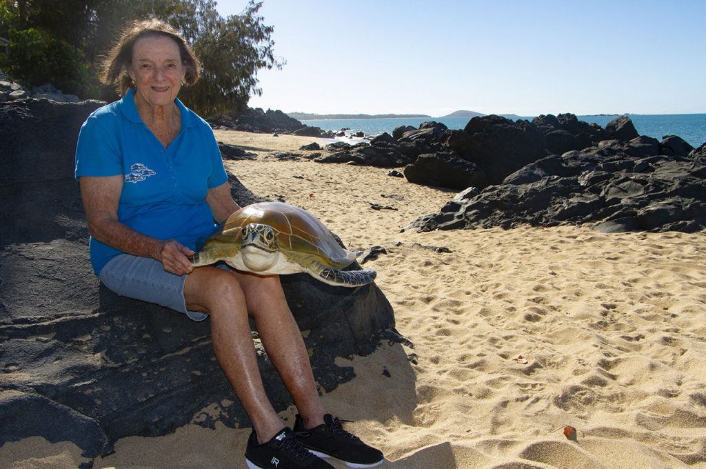 Woman sitting on a beach with a life sized turtle replica.