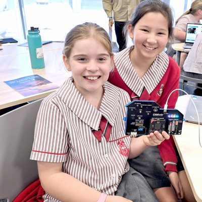 Two girls in school uniform hold up a Smart Sensor board