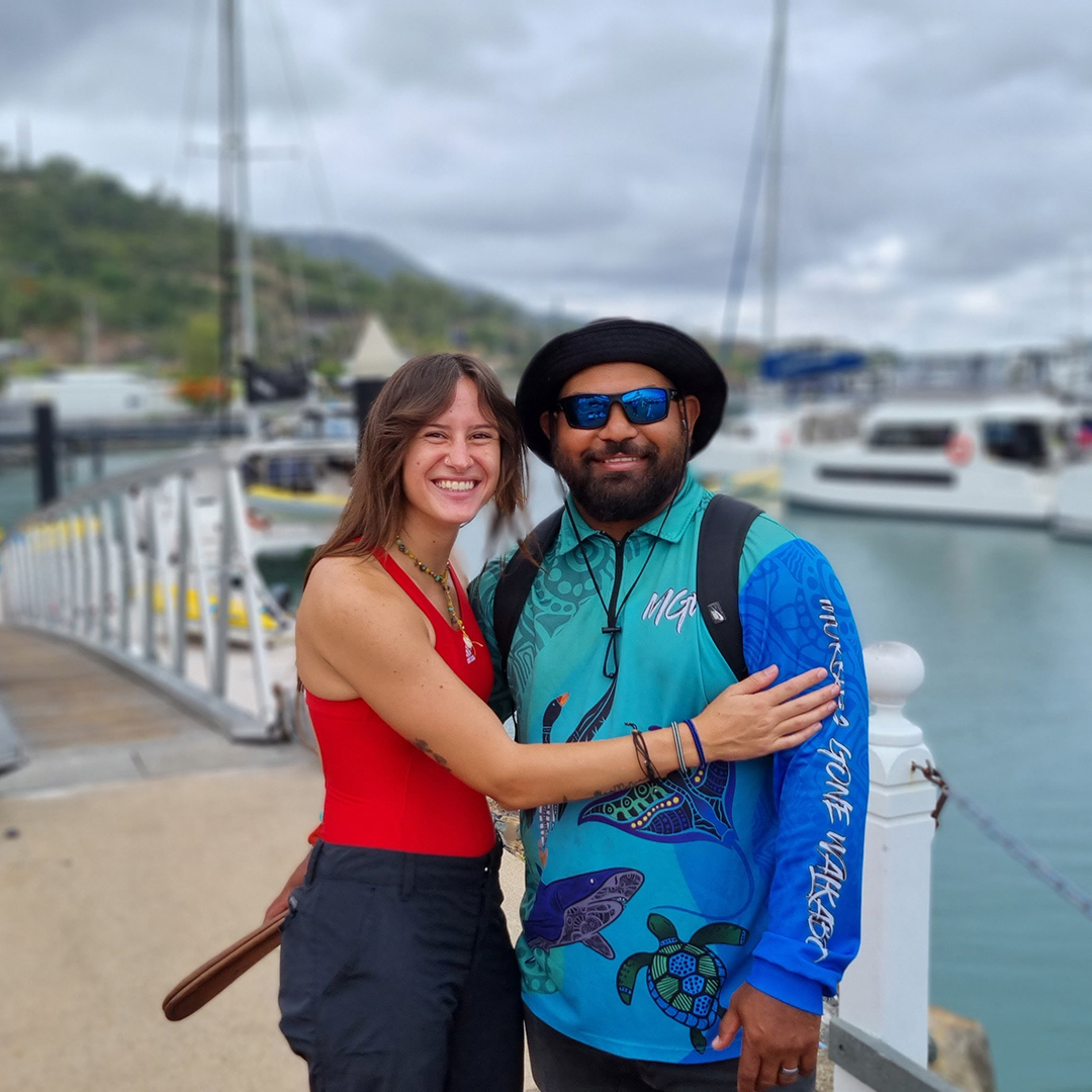 Two people standing on a dock in front of boats in water.