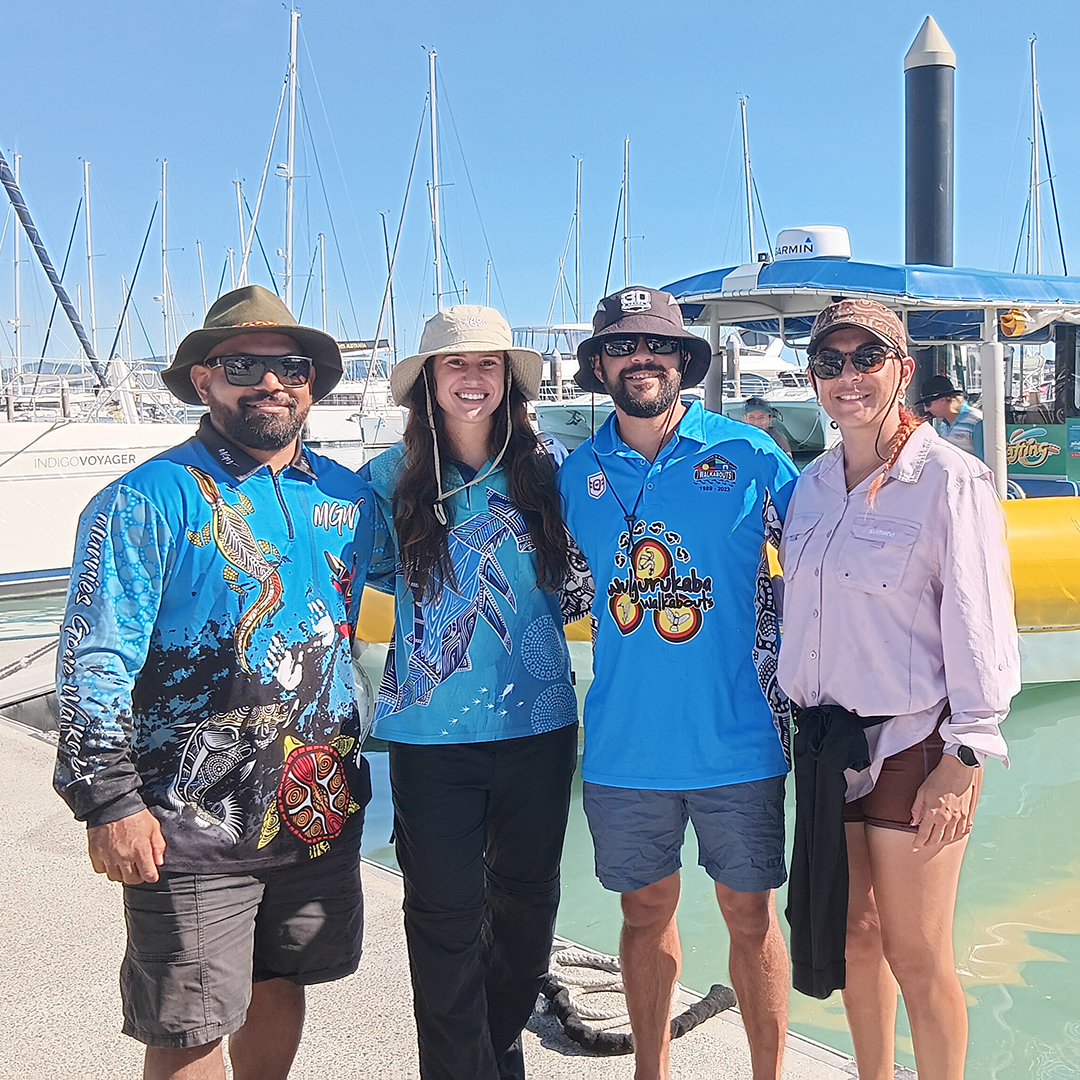 Four people standing on a dock in front of boats in water.