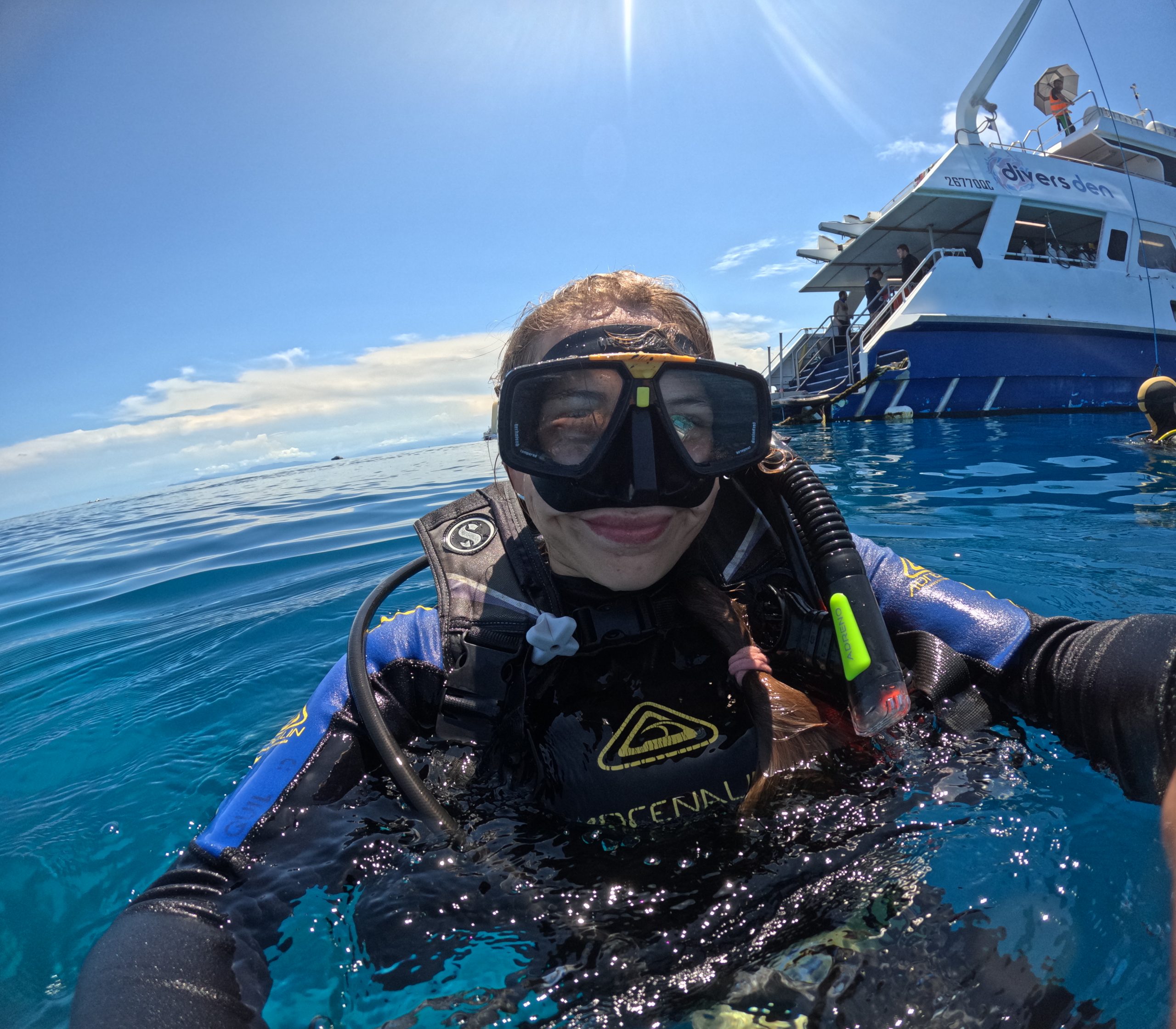 A woman is in the water with scuba gear, and boat is in the background.